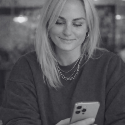 Outpost Social Co Maeve maeve bacon holding a mobile phone and smiling in black and white